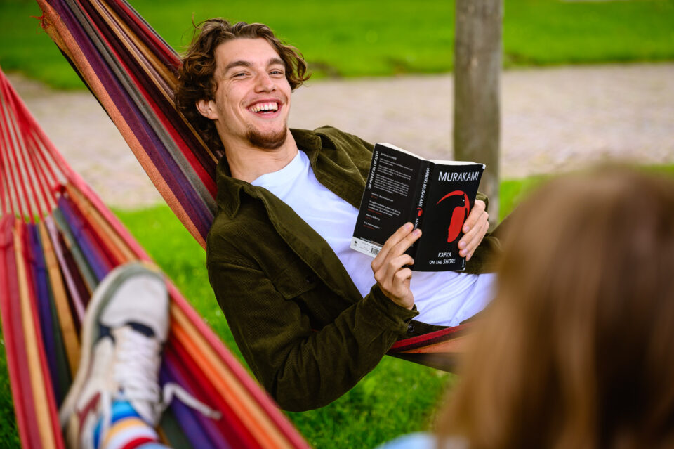 Deze jongen kijkt lachend omhoog terwijl hij in zijn hangmat leest. Een spontane momentopname van het studentleven op de Campus University Utrecht, ideaal voor de universiteit beeldbank en onderwijsmarketing.
