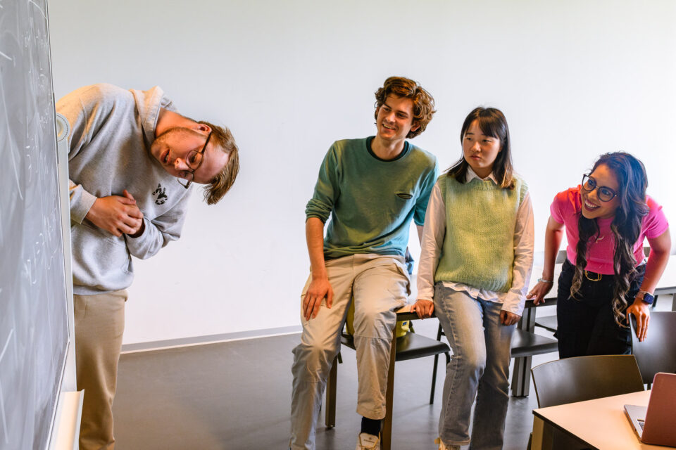 Terwijl de jongen zijn hoofd naar beneden draait, laat de andere student zich gaan met een uitbundige lach.