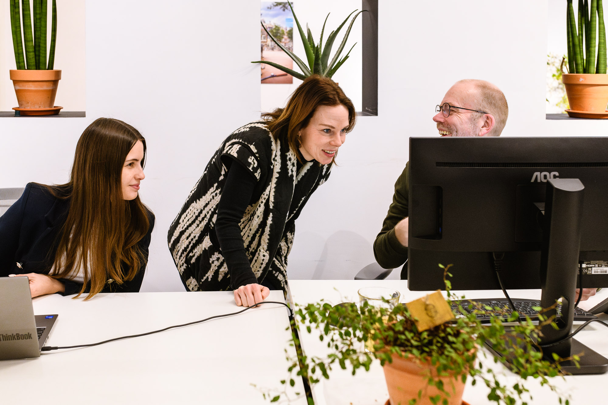 Drie collega's helpen elkaar. Een moment van samenwerking en collegialiteit, ideaal voor een branding kantoorreportage die de teamdynamiek benadrukt. Storytelling branding fotografie