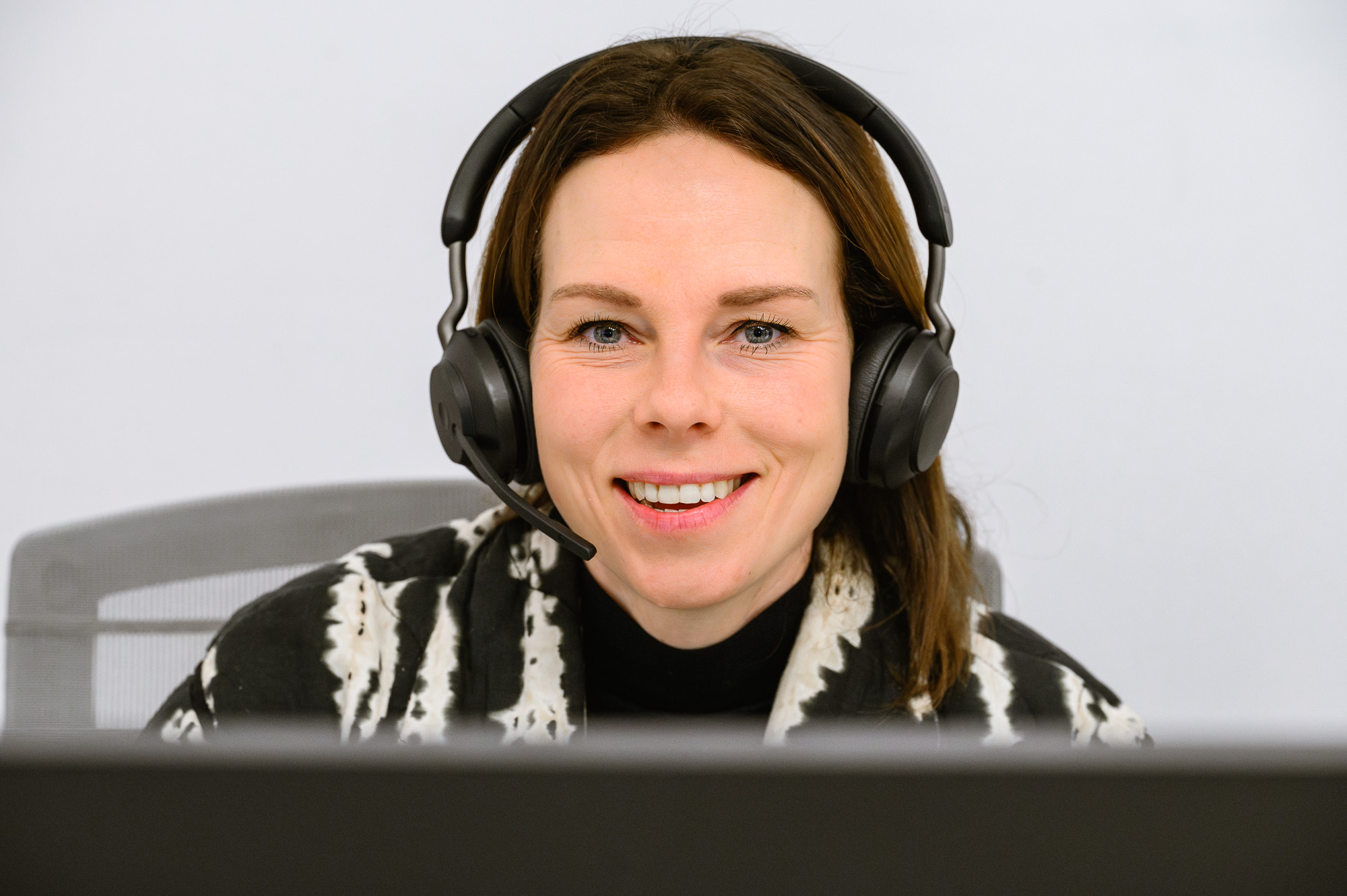 Lachende medewerker van de klantenservice, met koptelefoon op, vastgelegd tijdens een kantoorreportage in Amsterdam. Een spontaan moment dat de positieve sfeer en klantgerichte benadering benadrukt.